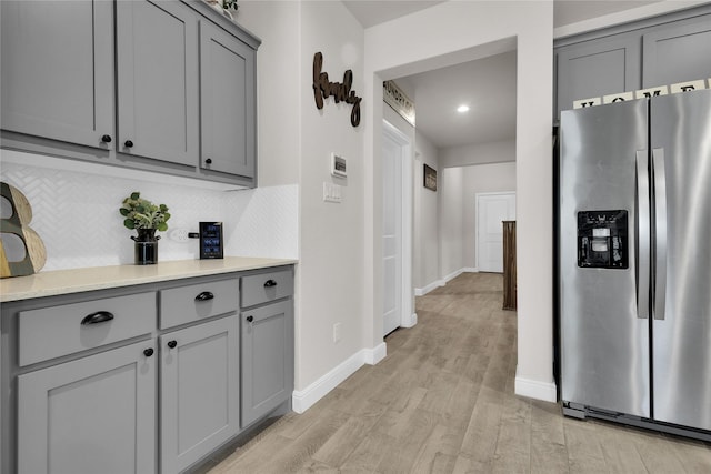 kitchen with stainless steel refrigerator with ice dispenser, gray cabinetry, backsplash, and light wood-type flooring