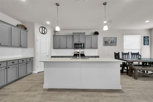 kitchen with sink, light hardwood / wood-style flooring, a kitchen island with sink, gray cabinetry, and decorative light fixtures