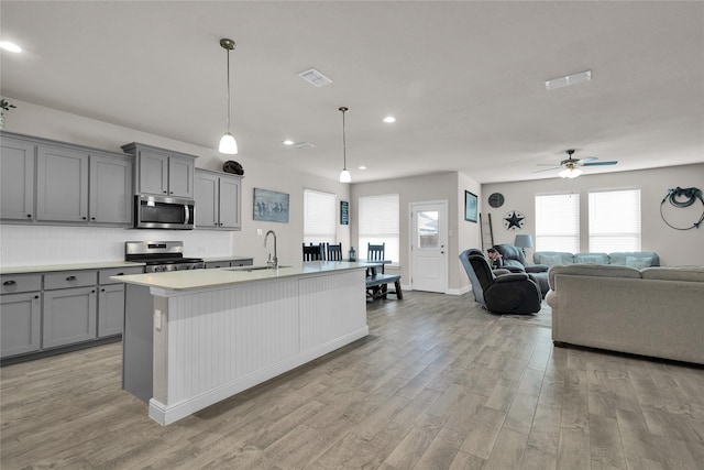 kitchen with pendant lighting, sink, light hardwood / wood-style flooring, stainless steel appliances, and a center island with sink