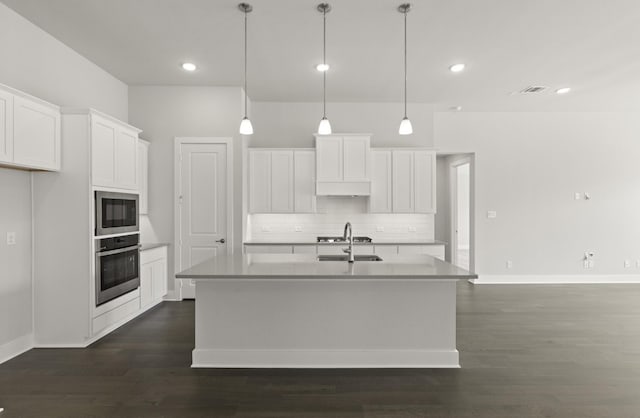 kitchen featuring built in microwave, oven, a center island with sink, and white cabinets