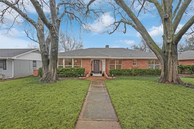 ranch-style home featuring a shingled roof, brick siding, a chimney, and a front lawn