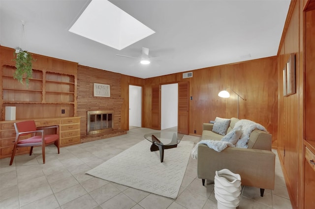 living room featuring a fireplace, a skylight, wood walls, light tile patterned floors, and built in shelves