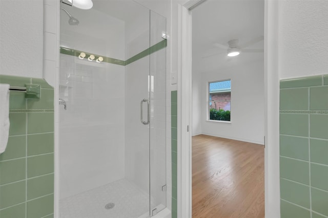 bathroom with tile walls, hardwood / wood-style flooring, a shower with shower door, and ceiling fan