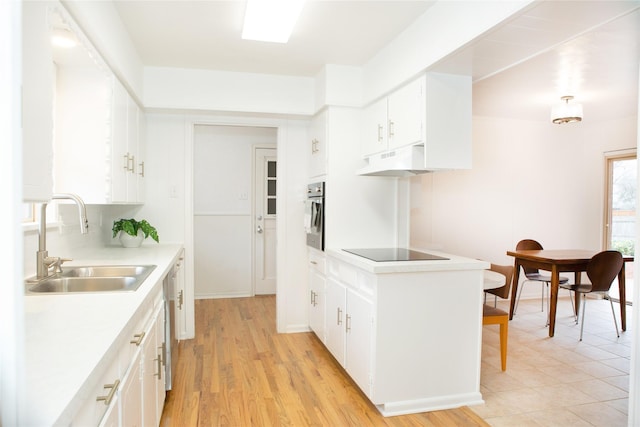 kitchen with a sink, light countertops, white cabinets, under cabinet range hood, and appliances with stainless steel finishes