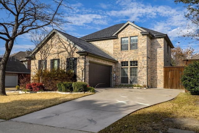 traditional-style house featuring an attached garage, brick siding, concrete driveway, roof with shingles, and a gate