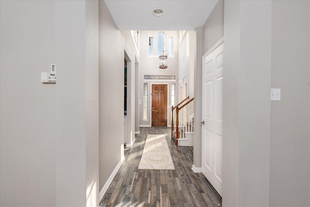 hallway with dark wood-type flooring, a high ceiling, stairway, and baseboards