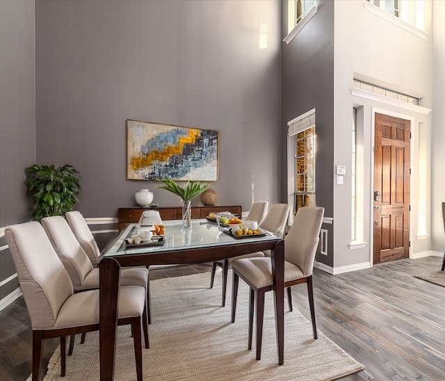 dining area featuring a towering ceiling, baseboards, and wood finished floors