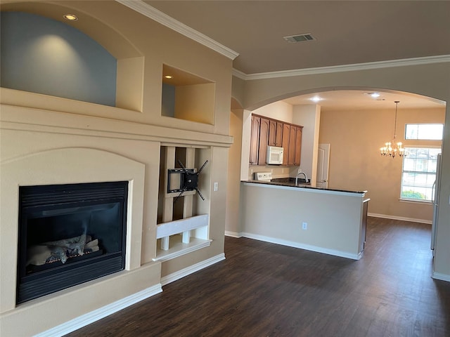 unfurnished living room with sink, crown molding, dark wood-type flooring, an inviting chandelier, and built in shelves