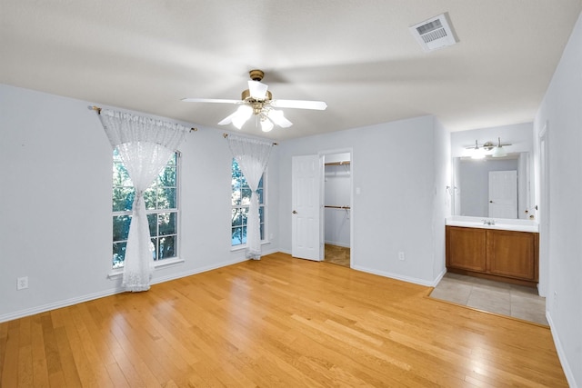 unfurnished bedroom with connected bathroom, a spacious closet, ceiling fan, light hardwood / wood-style floors, and a closet