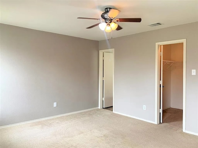 unfurnished bedroom with light carpet, a walk in closet, a closet, and ceiling fan