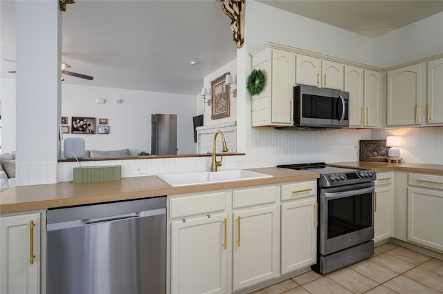 kitchen featuring appliances with stainless steel finishes, sink, light tile patterned floors, kitchen peninsula, and cream cabinetry