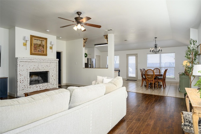 living room featuring dark wood-type flooring, ceiling fan with notable chandelier, and a tile fireplace