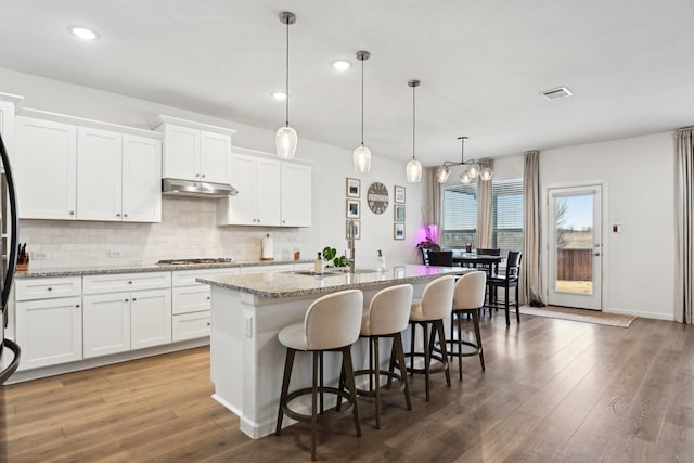 kitchen featuring a kitchen bar, an island with sink, hanging light fixtures, and white cabinets