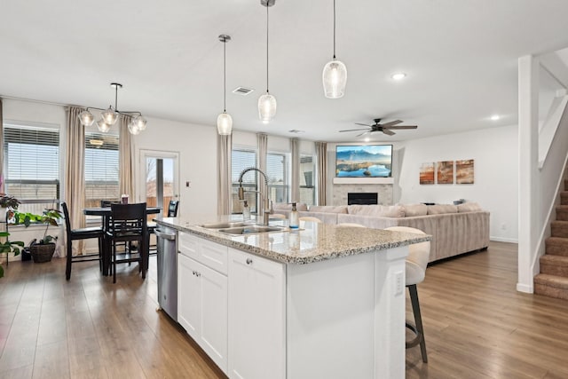 kitchen with white cabinetry, hanging light fixtures, sink, and a center island with sink