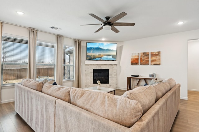 living room with ceiling fan, a stone fireplace, and hardwood / wood-style floors