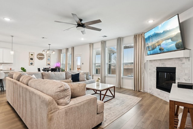 living room featuring ceiling fan, a stone fireplace, and light hardwood / wood-style floors