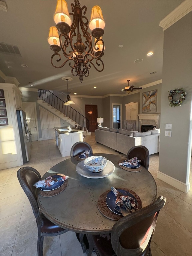 dining space featuring visible vents, stairway, ornamental molding, ceiling fan with notable chandelier, and a tile fireplace