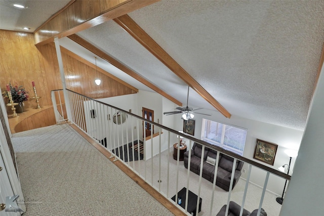 corridor with wooden walls, carpet, a textured ceiling, and vaulted ceiling with beams