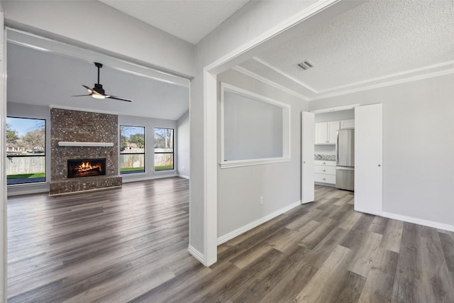 unfurnished living room featuring wood-type flooring, a large fireplace, ceiling fan, and a textured ceiling