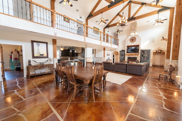 dining room with beamed ceiling, ceiling fan, a stone fireplace, and high vaulted ceiling