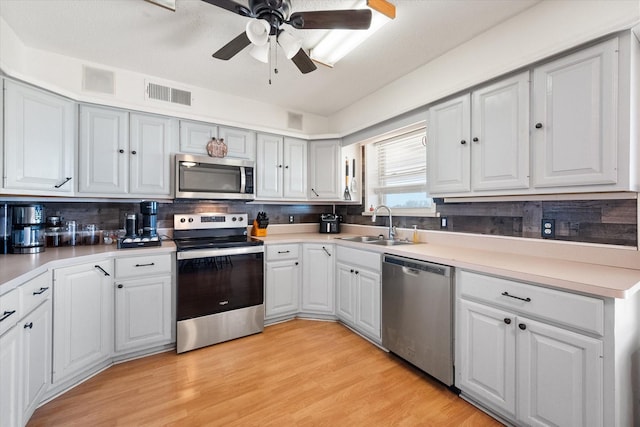 kitchen featuring sink, backsplash, appliances with stainless steel finishes, light hardwood / wood-style floors, and white cabinets