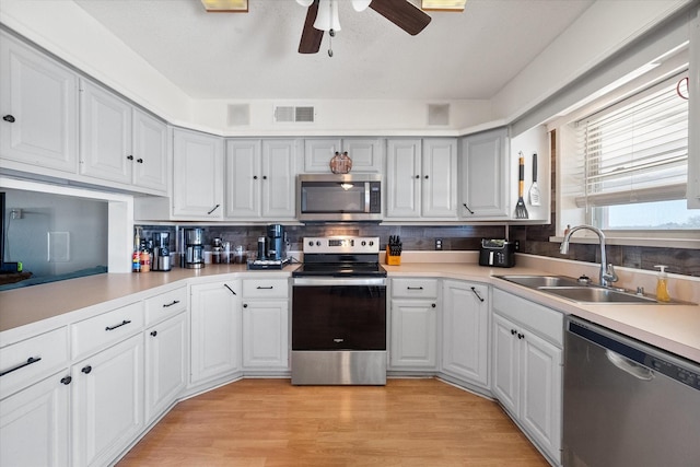 kitchen with sink, ceiling fan, appliances with stainless steel finishes, tasteful backsplash, and light hardwood / wood-style floors