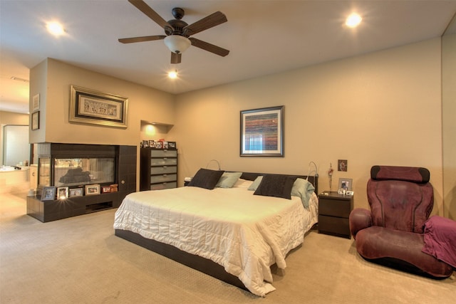 bedroom with a tile fireplace, light colored carpet, and ceiling fan