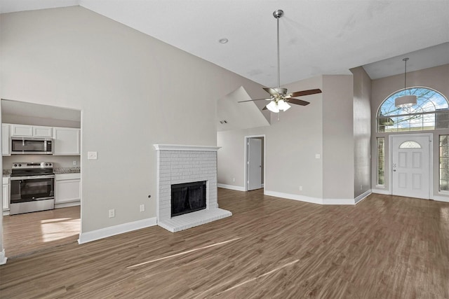 unfurnished living room with a brick fireplace, dark wood-type flooring, high vaulted ceiling, and ceiling fan