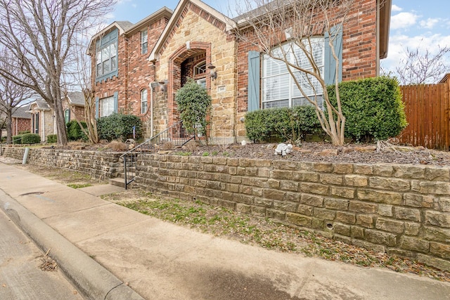 view of front facade with stone siding, brick siding, and fence