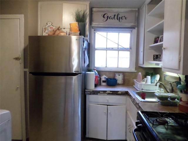 kitchen with white cabinetry, sink, stainless steel fridge, and gas stove