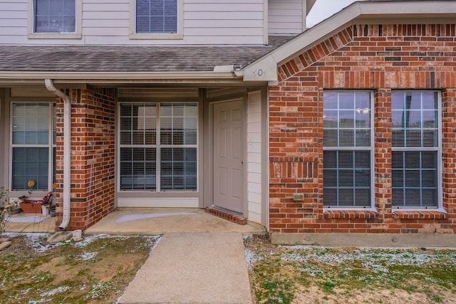 doorway to property with brick siding and roof with shingles