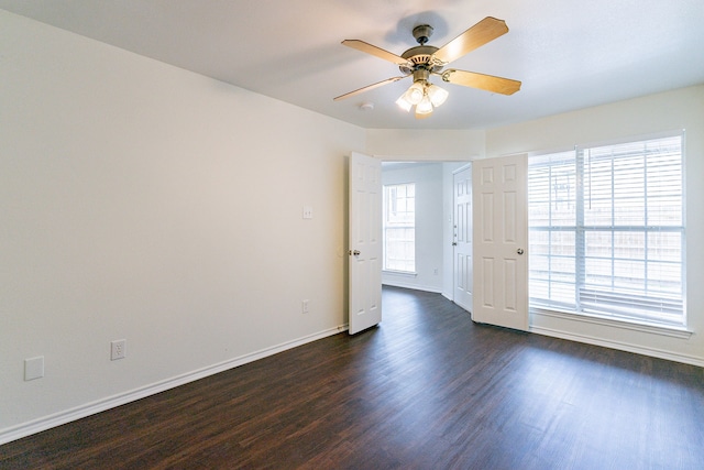 unfurnished room featuring baseboards, dark wood finished floors, and a ceiling fan