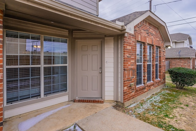 property entrance with roof with shingles and brick siding