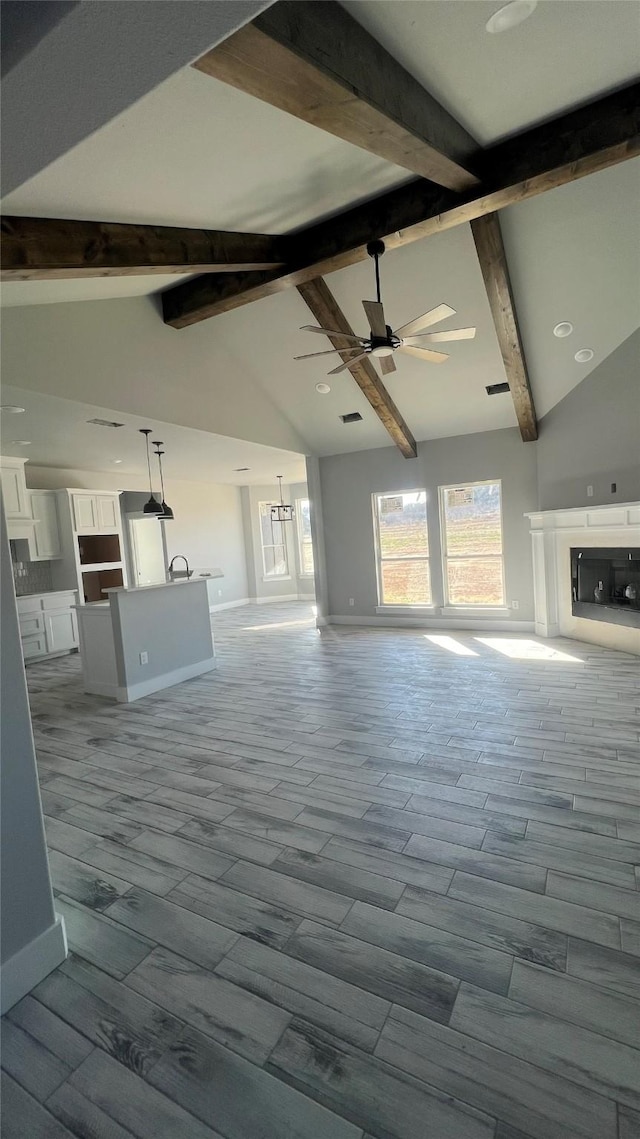 unfurnished living room with high vaulted ceiling, beam ceiling, and ceiling fan with notable chandelier