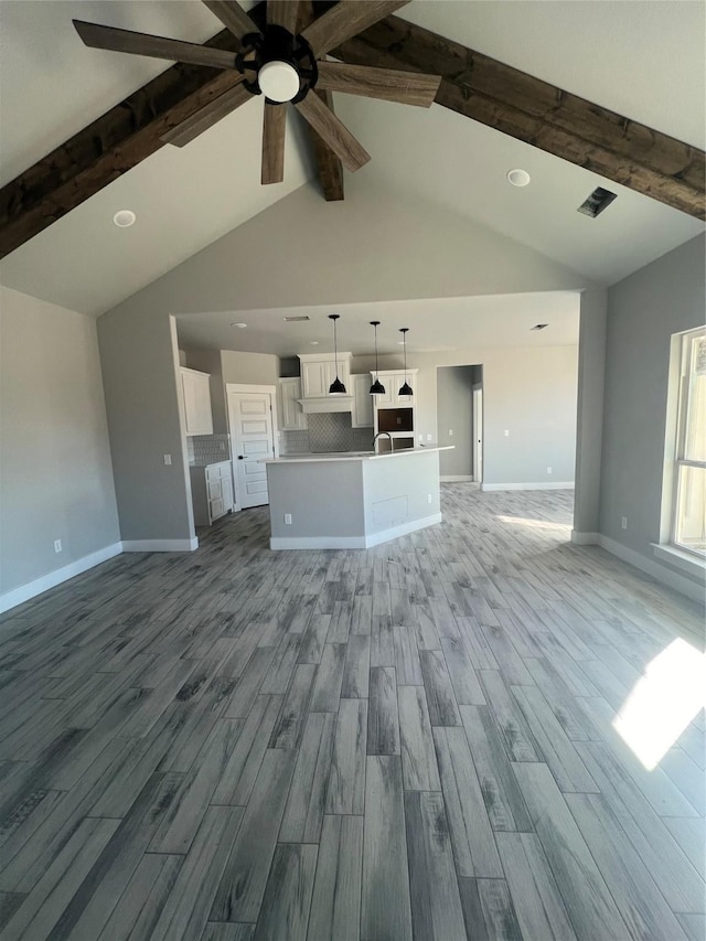 unfurnished living room featuring vaulted ceiling with beams, light hardwood / wood-style flooring, and ceiling fan