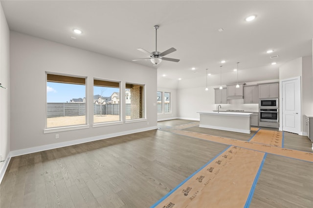 unfurnished living room featuring recessed lighting, a sink, light wood-style flooring, and baseboards