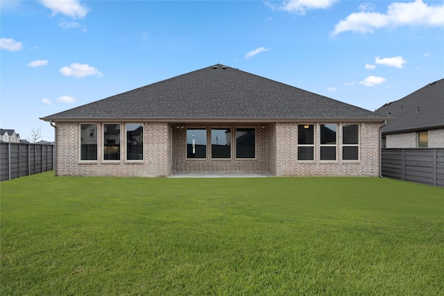 rear view of house featuring a shingled roof, brick siding, a yard, and a fenced backyard