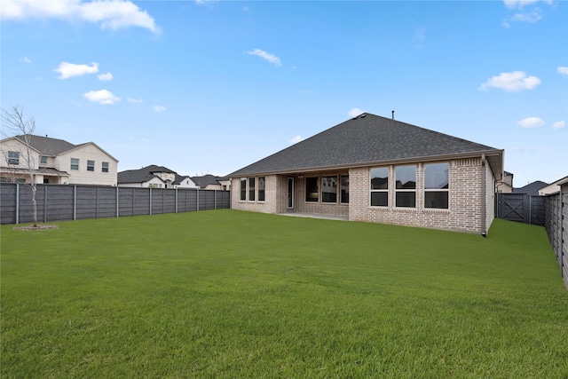 rear view of house featuring brick siding, a fenced backyard, roof with shingles, and a yard