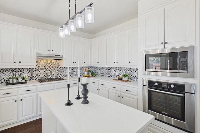 kitchen with appliances with stainless steel finishes, decorative light fixtures, white cabinetry, decorative backsplash, and a center island