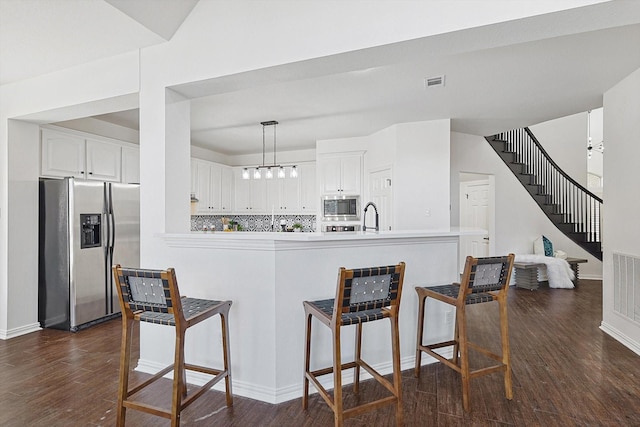 kitchen with white cabinetry, appliances with stainless steel finishes, dark hardwood / wood-style flooring, kitchen peninsula, and pendant lighting