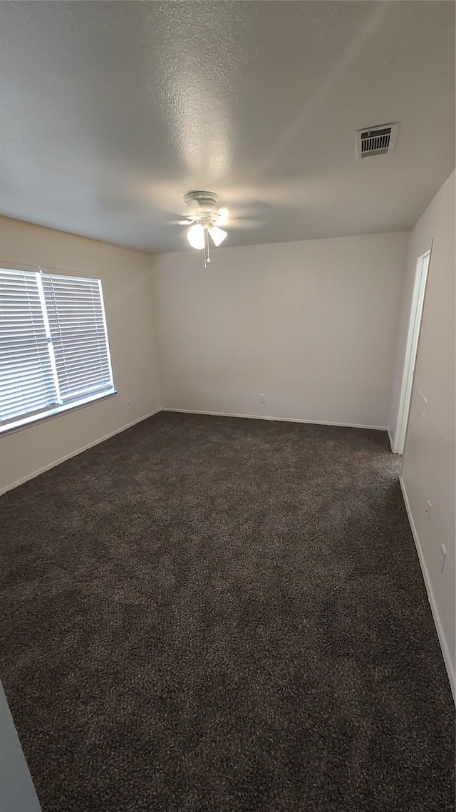 unfurnished room with ceiling fan, dark carpet, and a textured ceiling