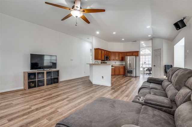 living room featuring a towering ceiling, ceiling fan, and light wood-type flooring