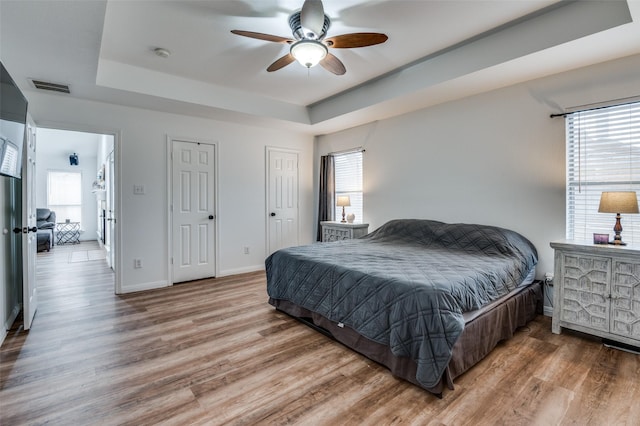 bedroom with a tray ceiling, wood-type flooring, and ceiling fan