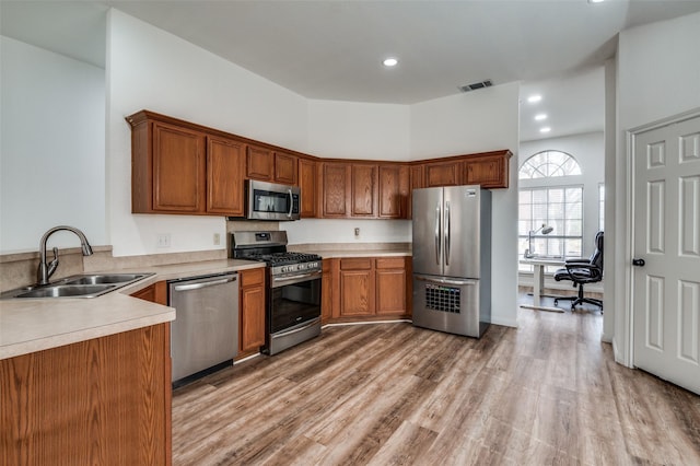 kitchen with sink, stainless steel appliances, light hardwood / wood-style floors, and a high ceiling