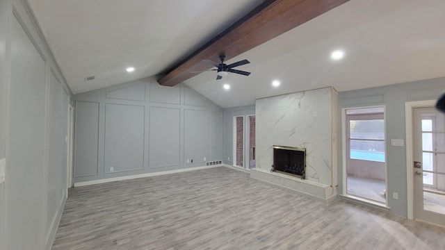 unfurnished living room with a high end fireplace, lofted ceiling with beams, ceiling fan, and light wood-type flooring