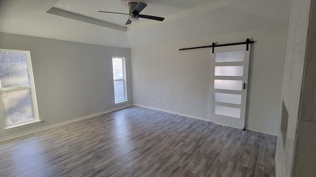 empty room with a raised ceiling, wood-type flooring, a barn door, and ceiling fan