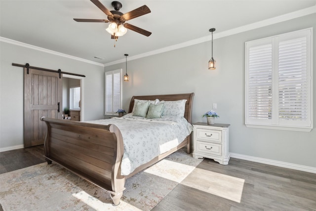 bedroom featuring crown molding, hardwood / wood-style flooring, ceiling fan, multiple windows, and a barn door