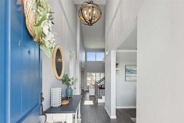 foyer entrance featuring dark wood-type flooring, a notable chandelier, crown molding, and a high ceiling