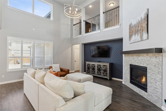 living room with a stone fireplace, a towering ceiling, a wealth of natural light, and dark hardwood / wood-style flooring