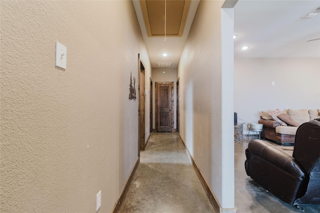 hallway with visible vents, a textured wall, concrete floors, and attic access